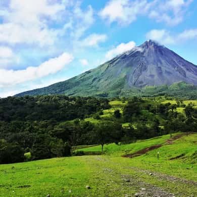 The cone of Arenal Volcano standing over green pasture and forest