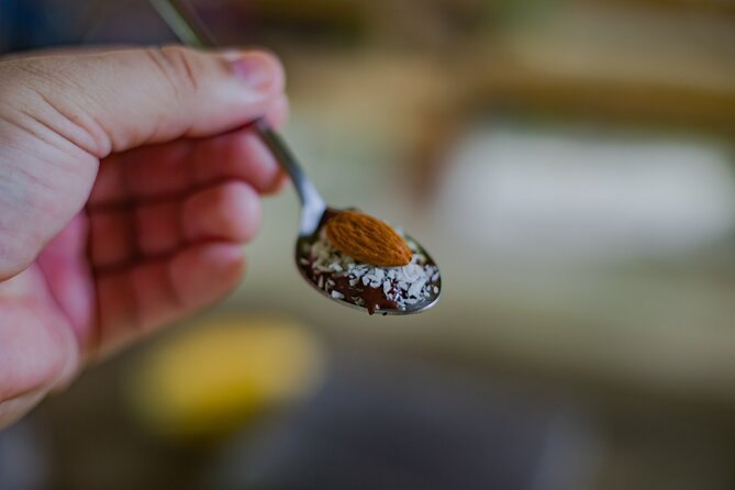 A spoonful of freshly ground cacao held over a cut pod